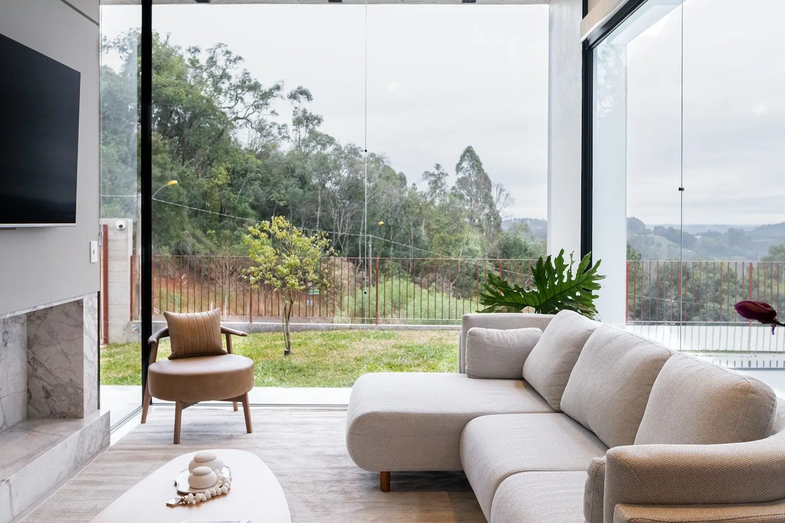 A living room with a board-marked concrete ceiling and a glass corner onto green hills