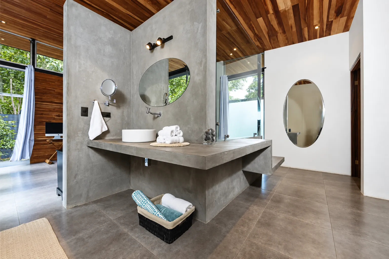 Open bathroom with a polished concrete wall, a floating vanity and round mirrors